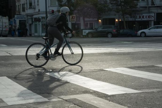 A bicyclist with a backpack and helmet is seen in the street adjacent to a crosswalk. 