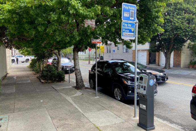 Cars outside near sidewalk with trees and parking meter pay station.