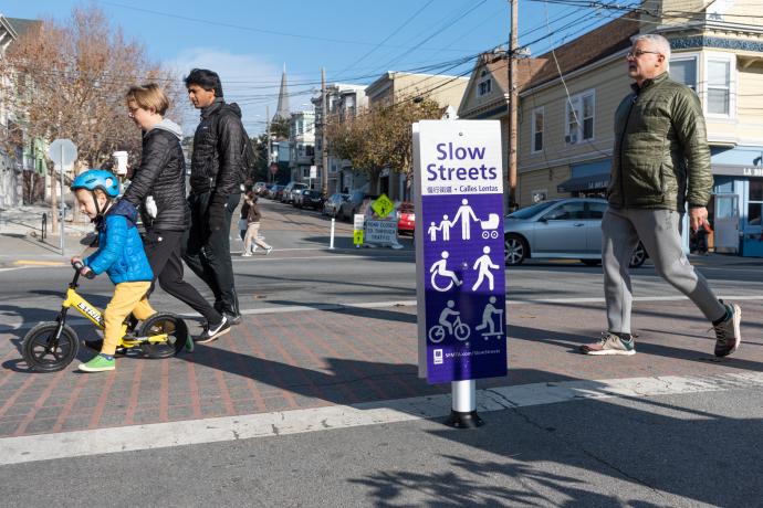 Slow Streets sign and people crossing the street