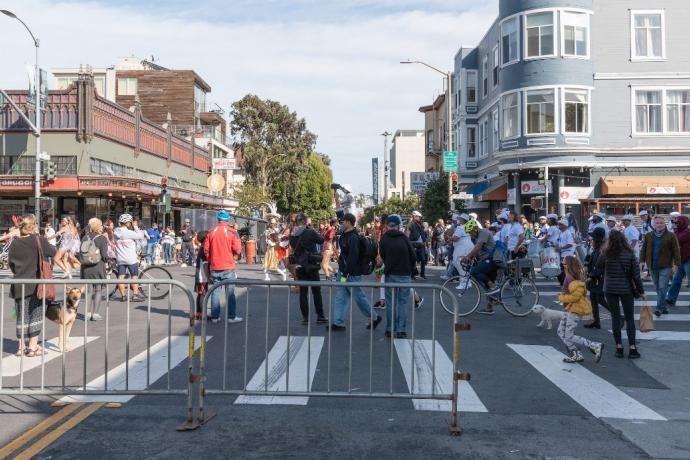 A large crowd of people at a street fair with blockades at the crosswalk.