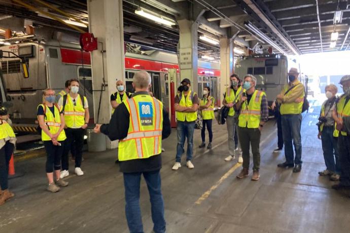 People are wearing safety vests inside a bus maintenance facility