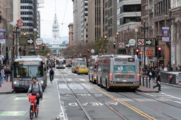 A view down Market Street toward the Ferry Building with taxis, buses and people bicycling and walking