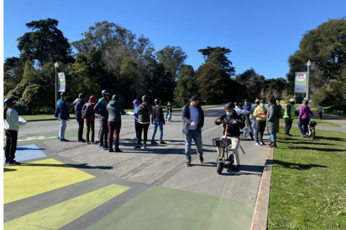 A group of people on a street with one riding an adaptive mobility scooter.