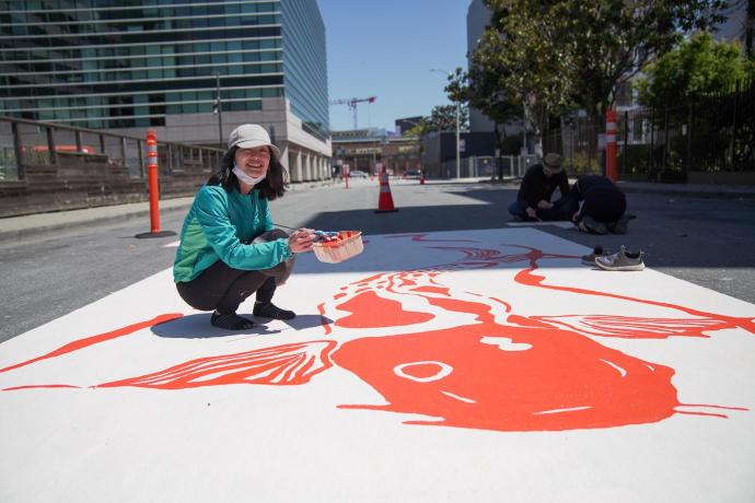 Photo of a community member painting a street mural on a SoMa Slow Street. Photo credit: Erina Alejo