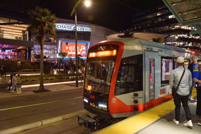 A light rail train stopped at a platform in front of the Chase Center arena in San Francisco.