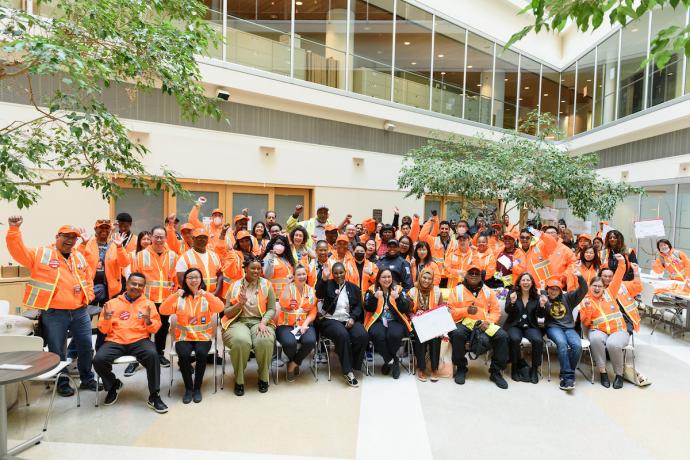 A group of SFMTA staff wearing orange and smile and wave to a camera.