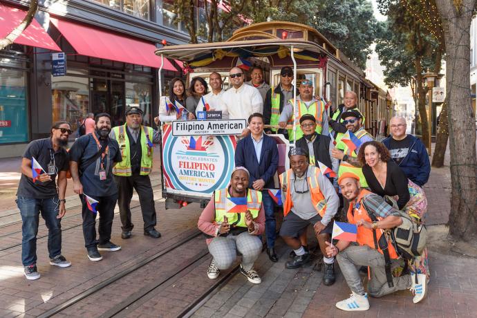 People standing and kneeling on and in front of a stationary cable car and on the tracks.