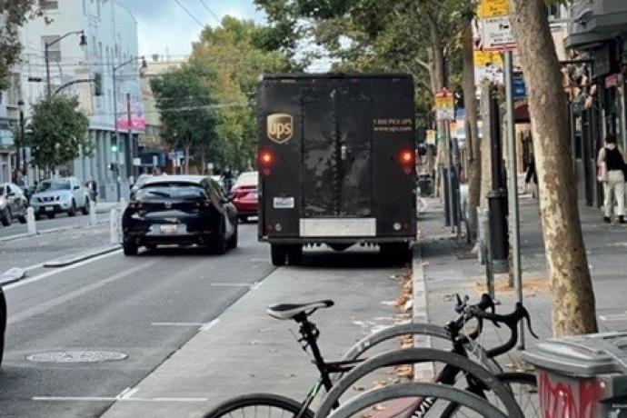 Parked bicycles on a sidewalk near cars and a delivery truck in a street. 