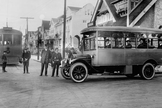 black and white image of people standing outside vintage bus and streetcar