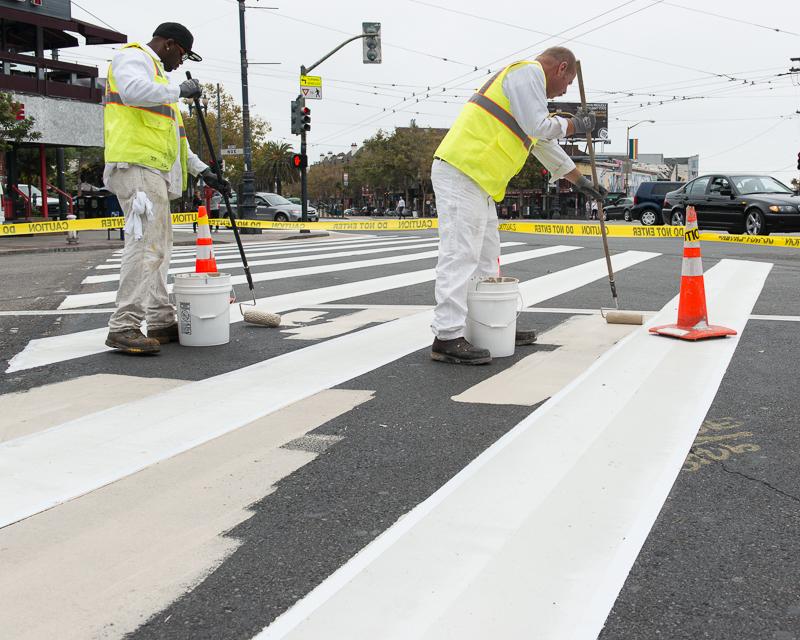 Painters apply paint to pavement in pedestrian safety zone at crosswalk