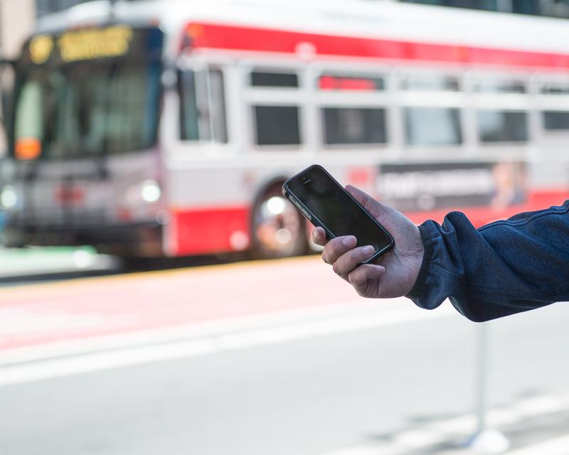 person's hand holding a smart phone with a Muni bus in the background