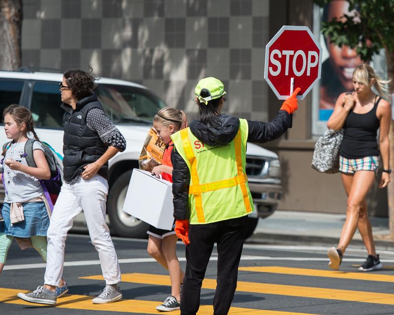 People crossing in crosswalk in front of crossing guard holding stop sign
