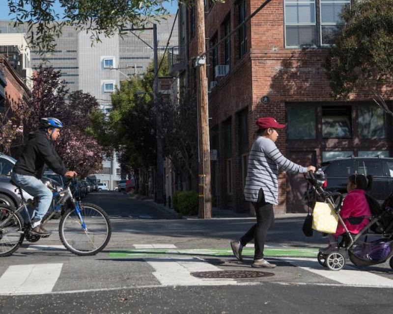 Pedestrian crossing Folsom and Sherman with a stroller with a biker in the bike lane.