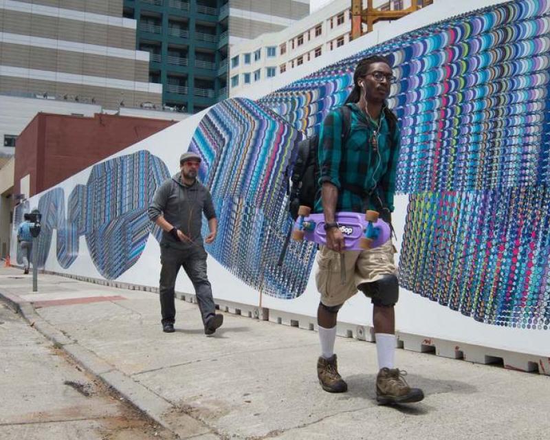 People walking on sidewalk in front of a mural 