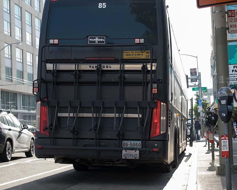 A shuttle bus is stopped at a street location reserved for shuttle buses as indicated by a sign