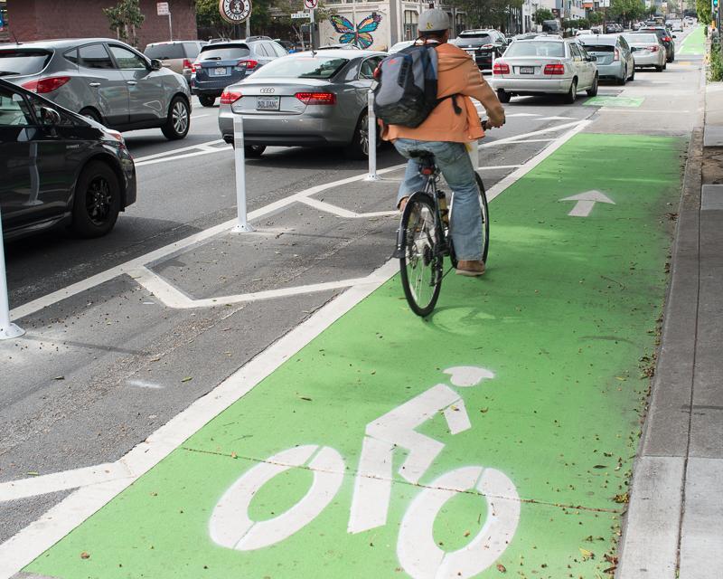 A person on a bike uses a protected green-color bike lane