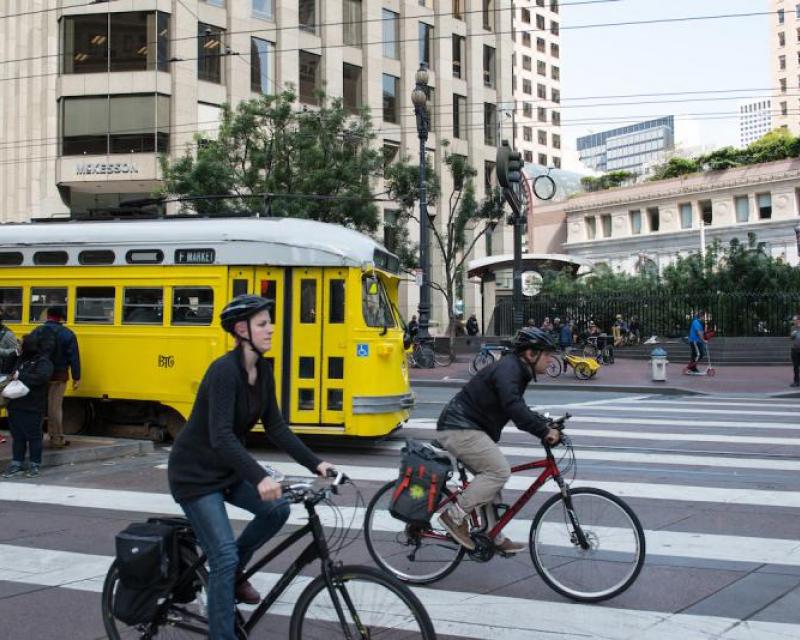 Two people riding bikes alongside a historic streetcar