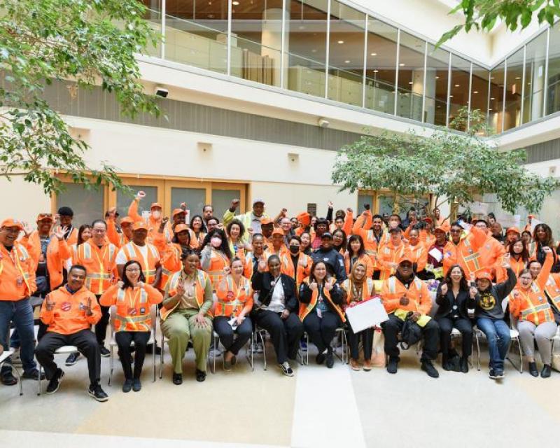 A large group of people dressed in orange vests wave for a picture.
