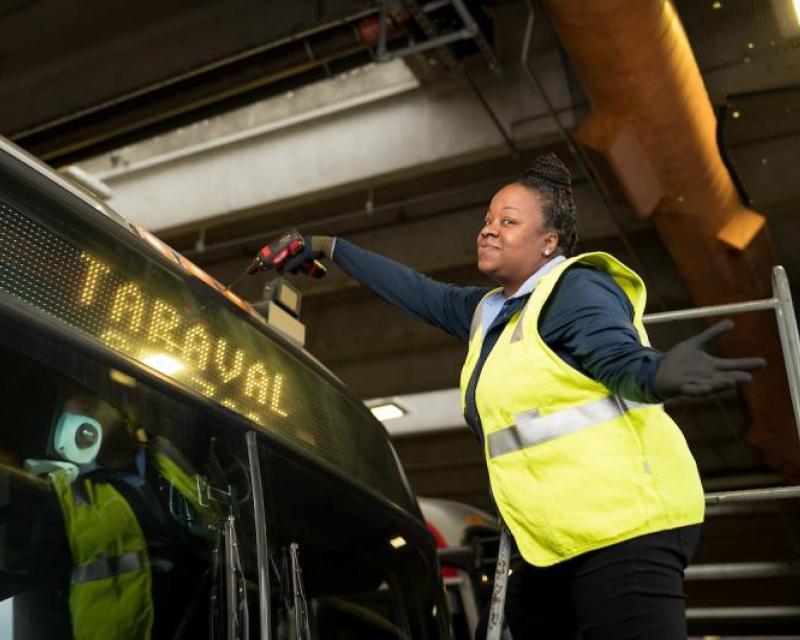 Nicole Humphrey changes a clearance light on a Muni bus. We see her with a drill, standing by the top of the bus.