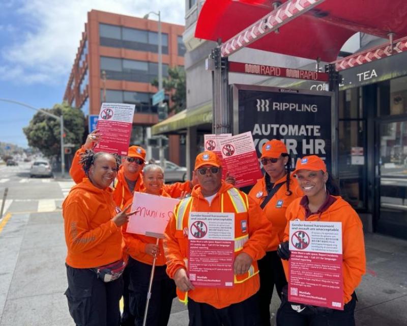 A group of people at a Muni bus stop holding signs about how to report harassment