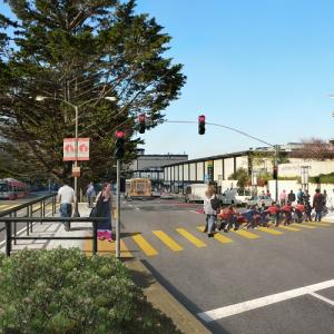 A visualization of Geary Boulevard at Buchanan Street with Geary Rapid improvements. People, including a chauffeured group school children, cross Geary using crosswalk that's separated into two sections by a waiting area in the median. Muni buses use red-colored, curbside transit-only lanes.