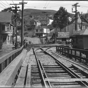 View north on Diamond near Chenery of wooden bridge and streetcar rails, street curving uphill and early 20th century buildings