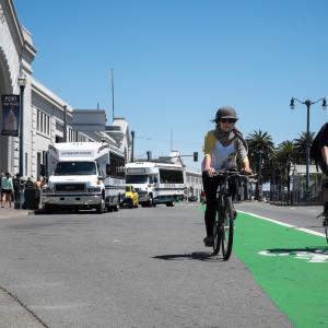 A person bicycling towards the camera in the green bike lane on the Embarcadero's roadway