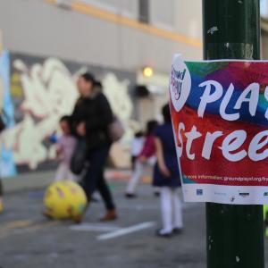 Play Streets event with colorful flyer in the foreground and children playing in the background