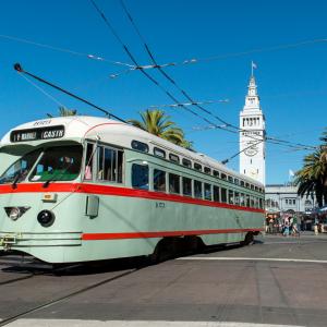 mint green streetcar with red striping and white roof in front of Ferry building on Market Street