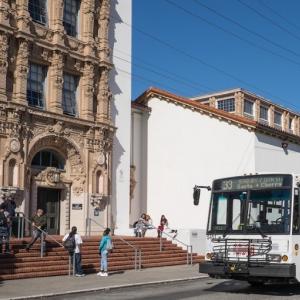 image of White and orange Muni trolley bus sits in front of Mission High School while students mingle