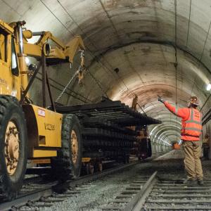 worker directing large machine lifting old track section inside Sunset Tunnel