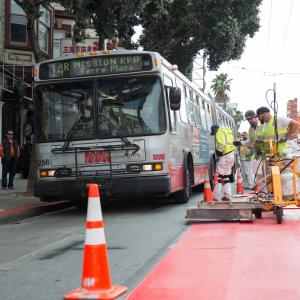 Crew placing red transit only lanes next to a 14R bus