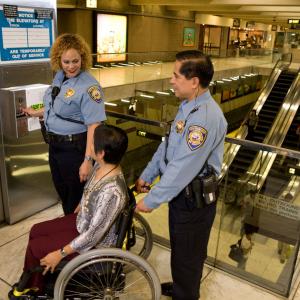 Image of two Muni safety officers helping a woman in a wheelchair into an elevator