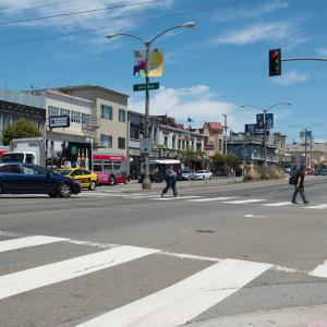 Photograph of Geary Boulevard at 4th Avenue where two pedestrians are crossing in the crosswalk while a car makes a left turn.