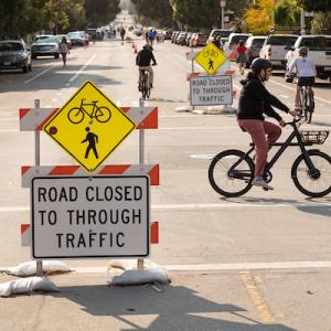 Image of temporary barriers in the travel lane stating "road closed to through traffic" with three bicyclists using the street