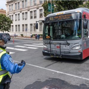 A traffic control officer guides a 49 Van Ness bus across an intersection