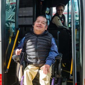 A customer in a wheelchair exits a bus while a driver deploys the lift