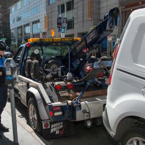 Photo of parking control officer issuing a citation while a tow truck prepares to tow away a van