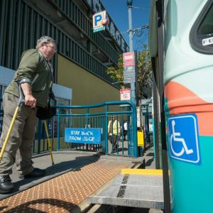 Bob Planthold boarding the F train via an accessibility ramp in his signature bright yellow crutches 