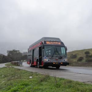 Muni bus parked on street with fog and hills behind.