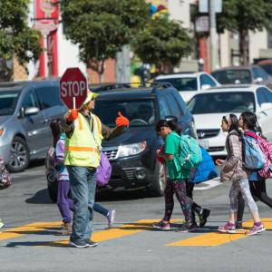 Crossing guard in the crosswalk holding a STOP sign with several children  walking 