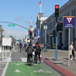 Bike riders and pedestrians seen on a city street's two-way bike lane at an intersection's red light