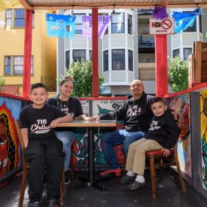 A family shown sitting in a colorful outdoor dining booth. 