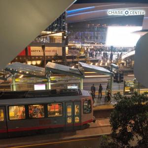  Photo of a Muni Metro train at the UCSF/Chase Center platform with Chase Center in the background.