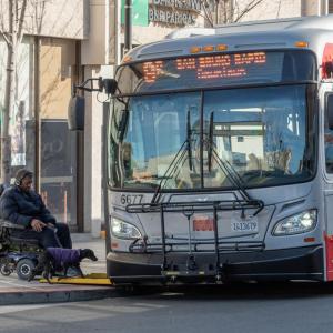 Image of a Muni bus pulled to the curb with its wheelchair ramp deployed as a transit rider using a wheelchair rolls onto bus 