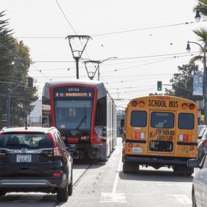 K Ingleside train running on Ocean Avenue as it crosses Faxon Avenue. Car traffic is present in front of and beh