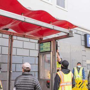  A picture containing contractors speaking with a Muni Rider as customer information displays are being installed in a transit s