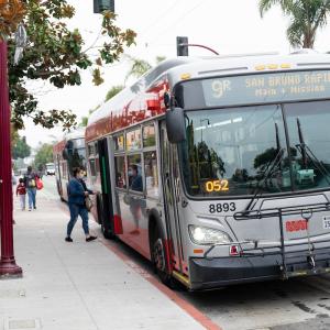 Person boarding a bus from a bus stop on the sidewalk with an adult and child walking down the street.