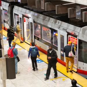 People walking on a station platform. Some are boarding. Some are deboarding. 