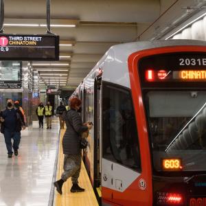 A train is pulled up alongside a metro station platform. One passenger is seen boarding. 
